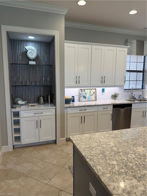 Kitchen with white cabinetry, ornamental molding, light stone countertops, dishwashing machine, and decorative backsplash