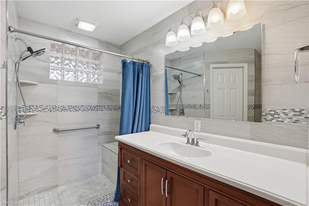 Bathroom with vanity, a shower stall, and tile walls