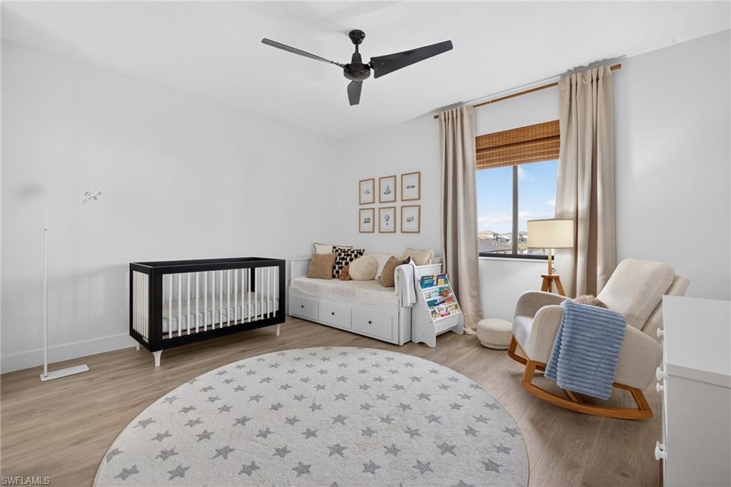 Bedroom featuring a crib, light wood-style floors, and a ceiling fan