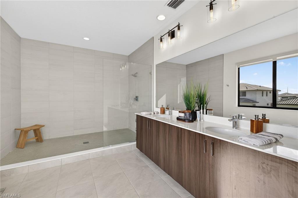 Bathroom featuring walk in shower, double vanity, light tile patterned floors, and recessed lighting