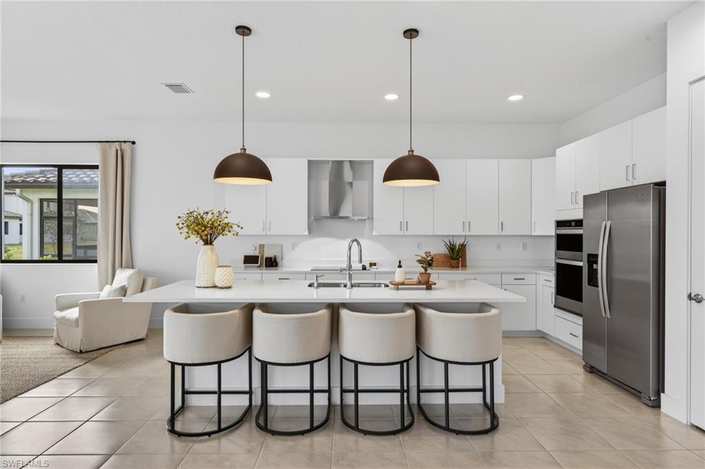 Kitchen with stainless steel appliances, white cabinetry, decorative light fixtures, and a center island with sink