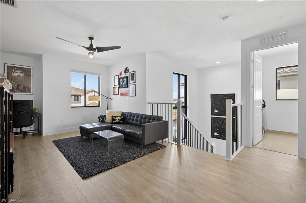 Living room with a desk, light wood-type flooring, a ceiling fan, and a textured ceiling