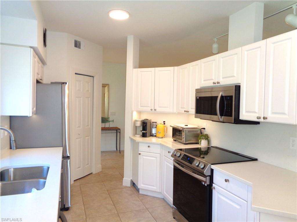Kitchen with stainless steel appliances, white cabinetry, light tile patterned flooring, and light stone countertops
