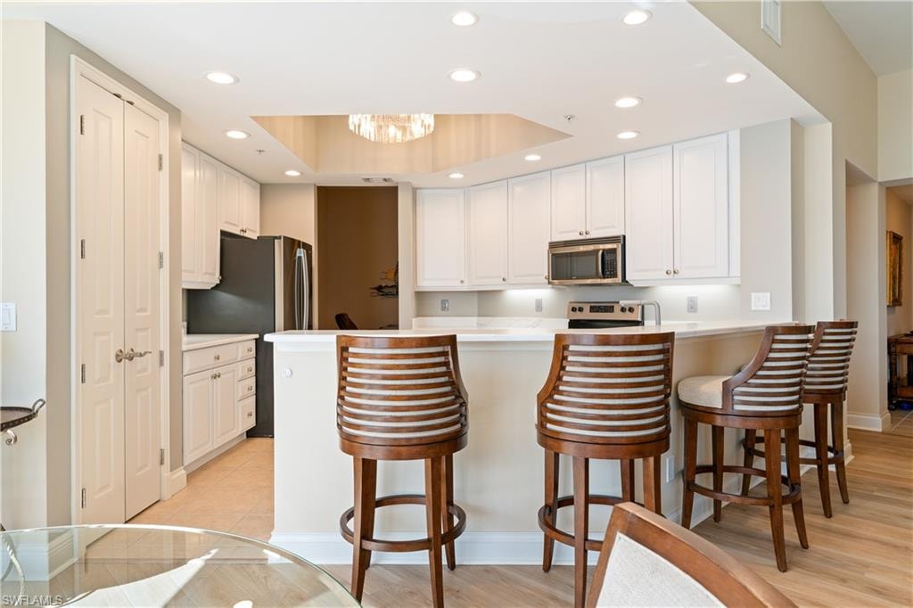 Kitchen with a kitchen bar, a peninsula, white cabinetry, and light countertops