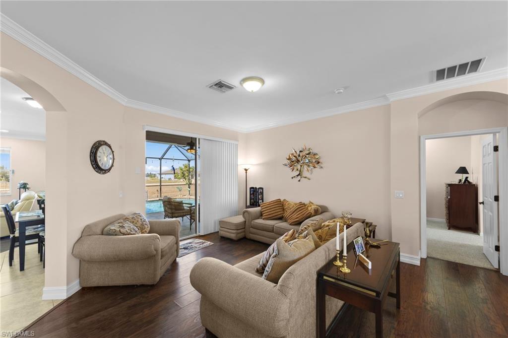 Living room featuring arched walkways, a sunroom, dark wood-style flooring, and crown molding