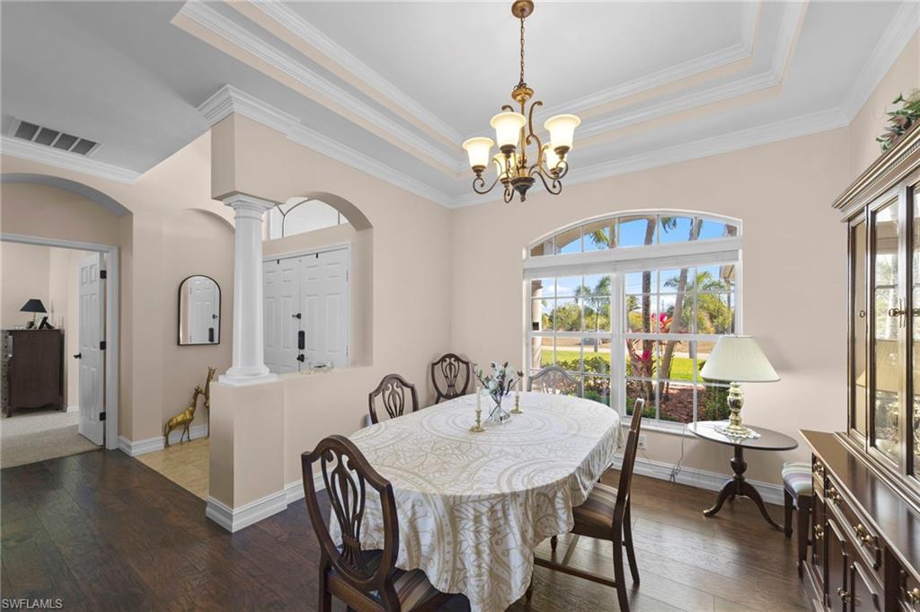 Dining room with a raised ceiling, wood-type flooring, ornamental molding, arched walkways, and hanging lights