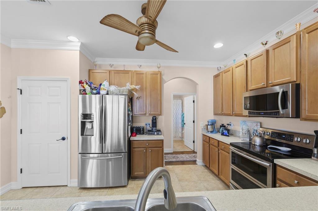 Kitchen with stainless steel appliances, arched walkways, light countertops, ceiling fan, and ornamental molding