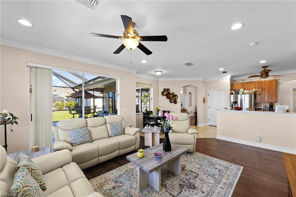 Living room with a ceiling fan, ornamental molding, arched walkways, dark wood finished floors, and recessed lighting