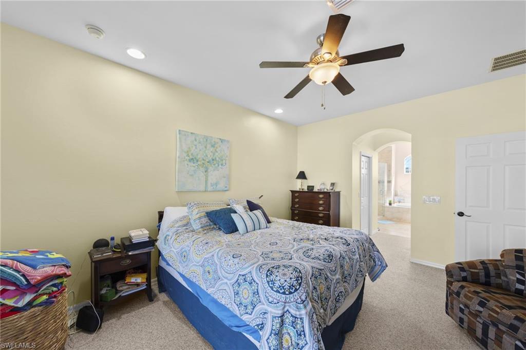 Bedroom with arched walkways, light carpet, a ceiling fan, and ensuite bath