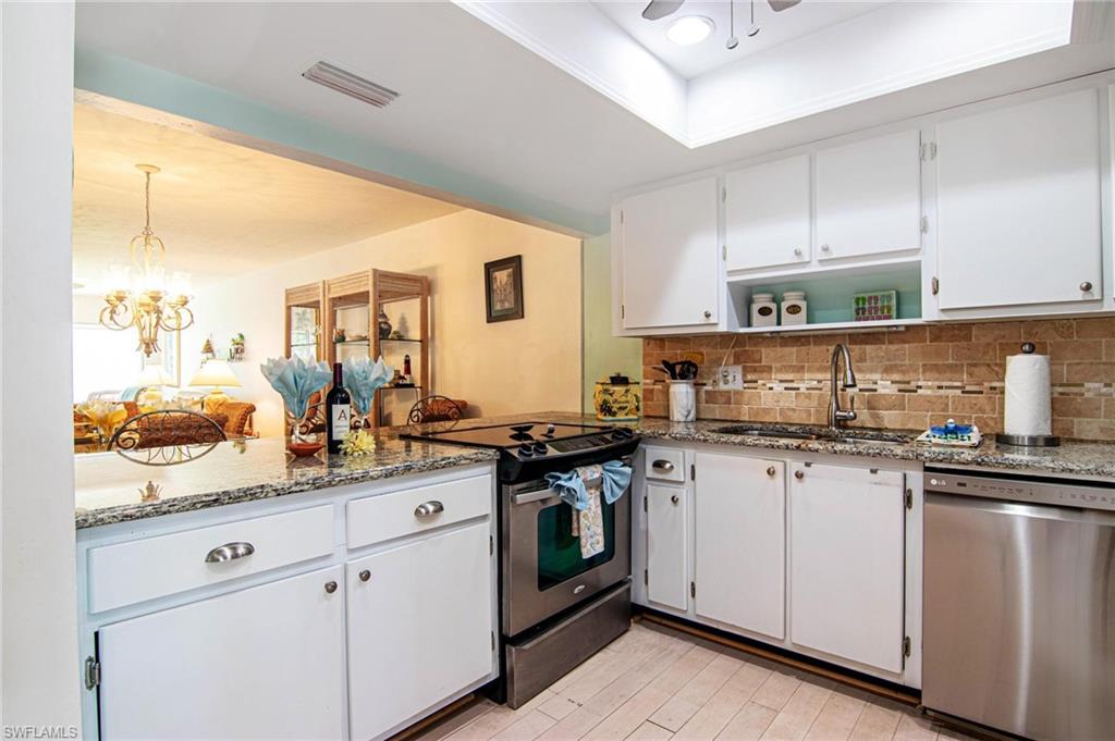 Kitchen featuring white cabinetry, stainless steel appliances, light stone countertops, tasteful backsplash, and a chandelier