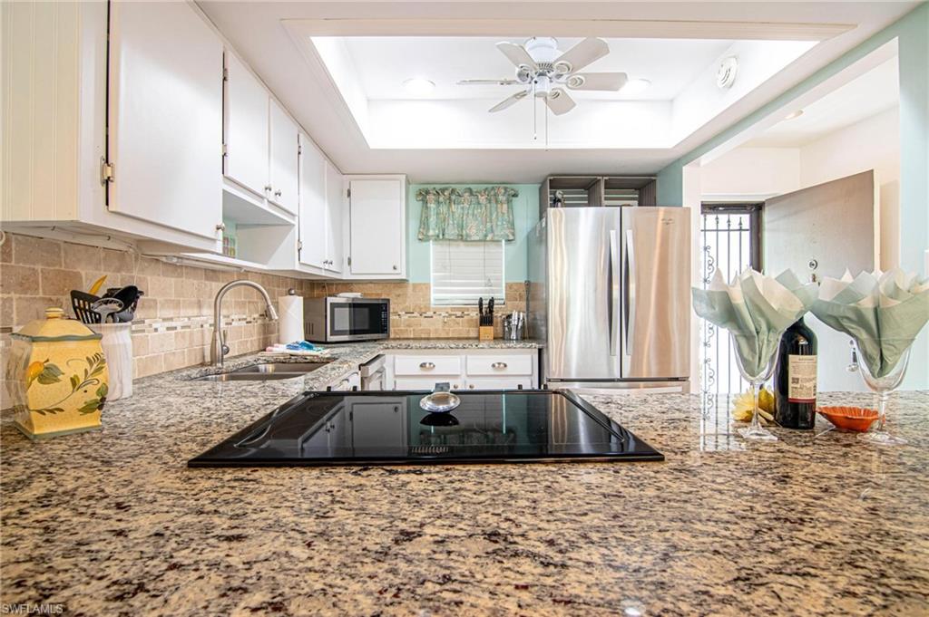 Kitchen with stainless steel appliances, white cabinets, a ceiling fan, a raised ceiling, and light stone counters