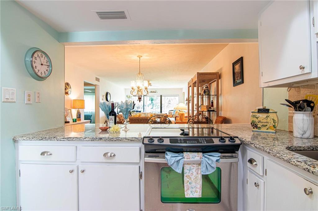 Kitchen featuring stainless steel electric stove, a peninsula, white cabinets, and light stone counters