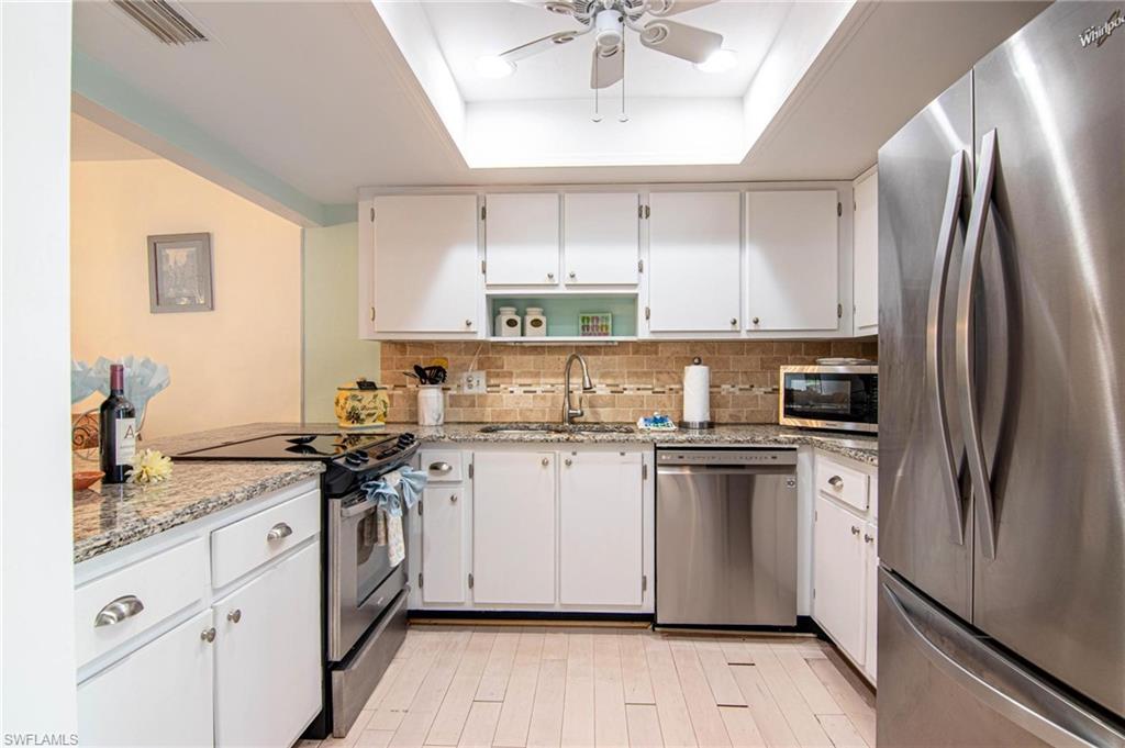 Kitchen featuring stainless steel appliances, white cabinetry, ceiling fan, open shelves, and light stone counters