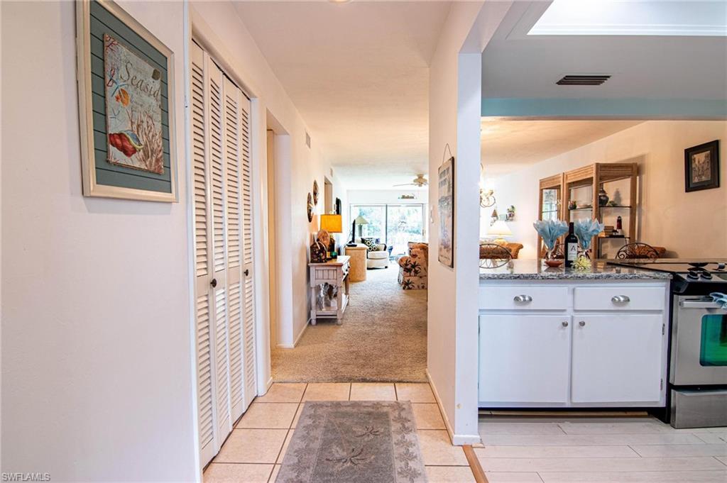 Kitchen featuring stainless steel electric range oven, dark stone counters, light tile patterned flooring, open floor plan, and white cabinets