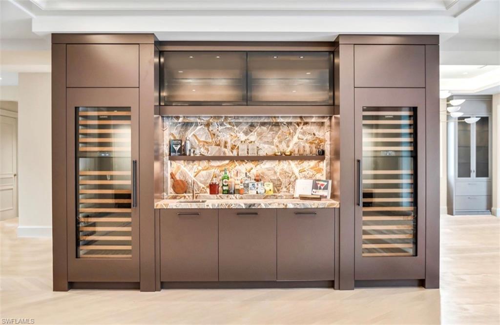 Built-in wet bar featuring stone backsplash, 2 integrated Subzero wine refrigerators, under-cabinet lighting, and custom cabinetry with hardware