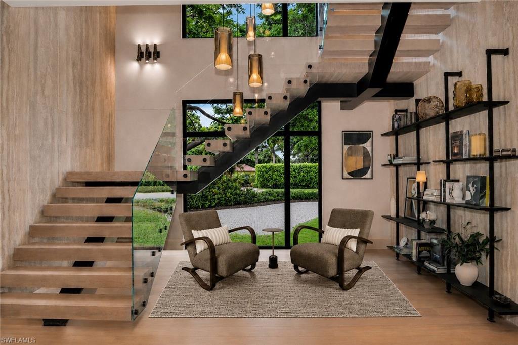 One-of-a-kind, unparalleled design staircase featuring imported travertine walls, custom lime wash window wall and ceiling, Italian leaning bookshelf, a Penta light fixture from Italy, and custom chairs from Bali. Only furniture, rug, and exterior paving stones added with AI