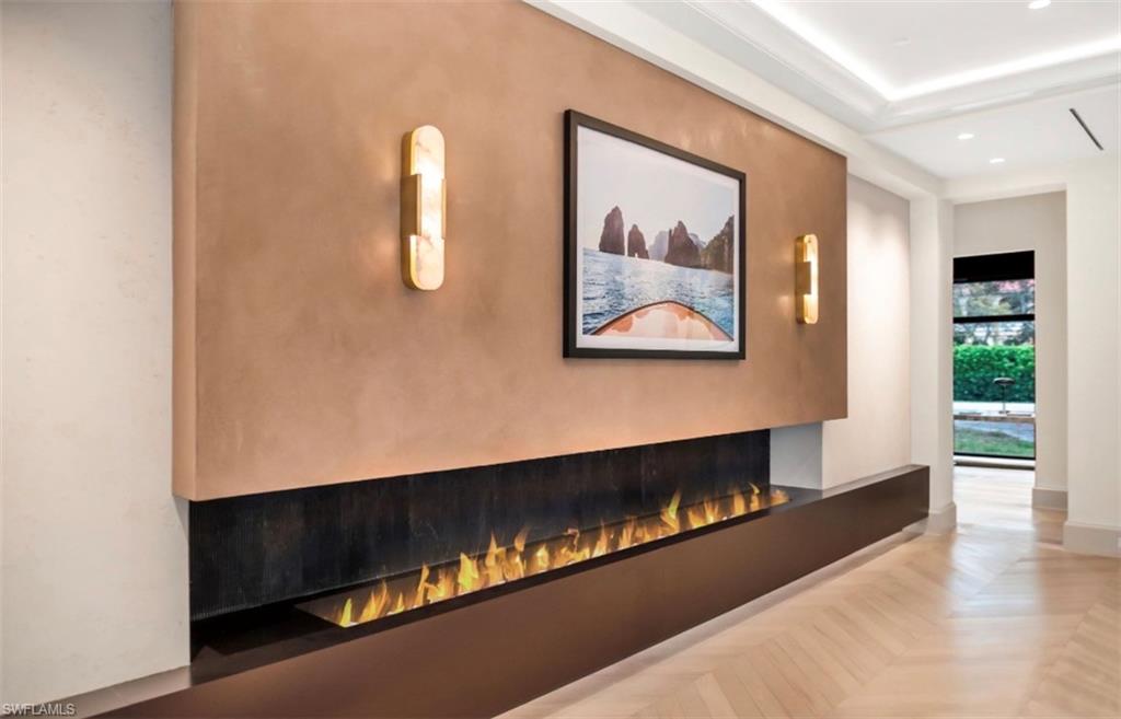 Linear gas fireplace, chevron wood flooring, Venetian plaster accent wall, and lit tray ceiling