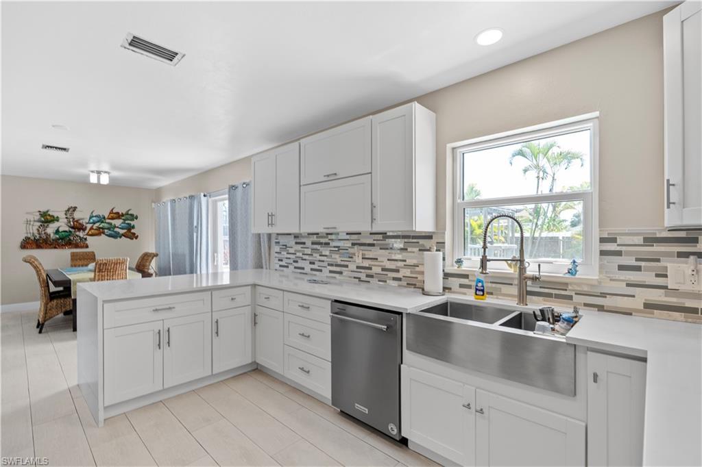 Kitchen featuring a peninsula, dishwasher, white cabinetry, backsplash, and light stone counters
