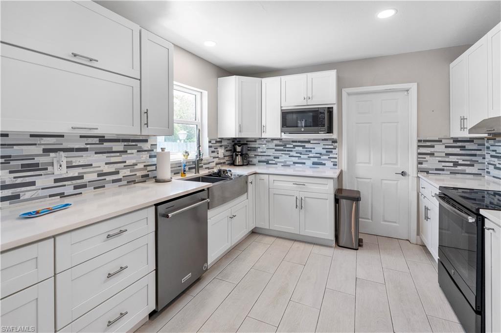 Kitchen with white cabinets, stainless steel appliances, light stone counters, recessed lighting, and decorative backsplash