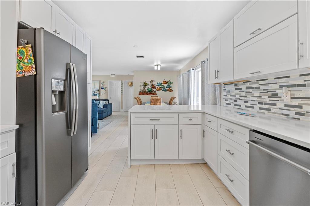 Kitchen featuring stainless steel appliances, white cabinets, a peninsula, open floor plan, and backsplash