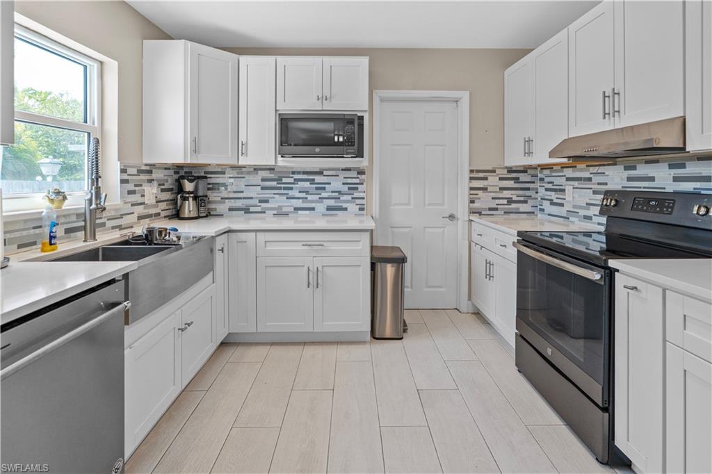 Kitchen featuring stainless steel appliances, white cabinetry, light wood-type flooring, backsplash, and light stone counters