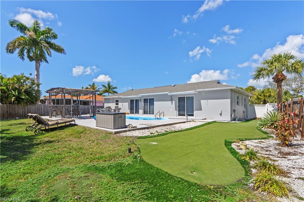 Back of property featuring a patio, a fenced backyard, a pergola, stucco siding, and a putting green