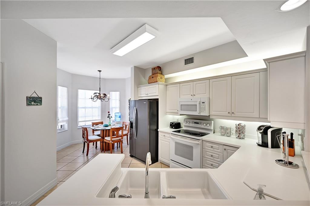 Kitchen featuring white appliances, light countertops, a chandelier, light tile patterned flooring, and white cabinetry