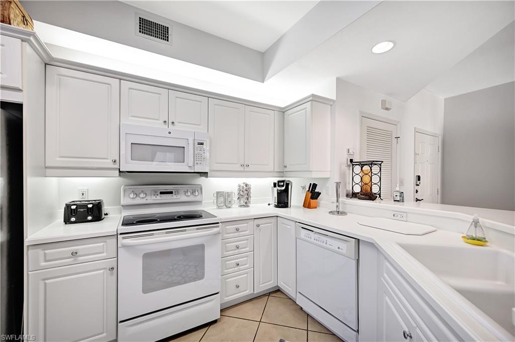 Kitchen with white appliances, light countertops, white cabinets, and light tile patterned flooring