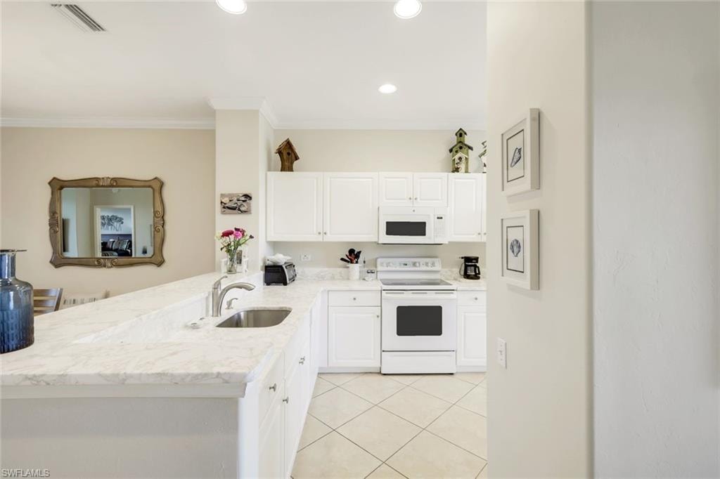 Kitchen featuring white appliances, white cabinets, a peninsula, light stone countertops, and light tile patterned flooring