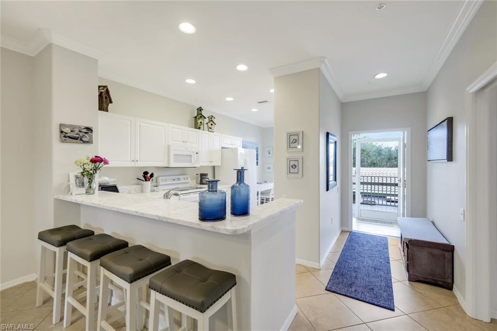 Kitchen with a breakfast bar area, a peninsula, white cabinetry, white appliances, and recessed lighting