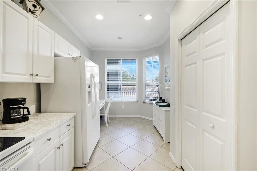 Kitchen with white cabinets, ornamental molding, white appliances, light tile patterned floors, and light stone counters