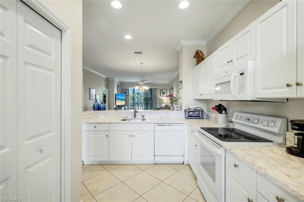 Kitchen with white appliances, ornamental molding, a chandelier, light stone countertops, and white cabinetry