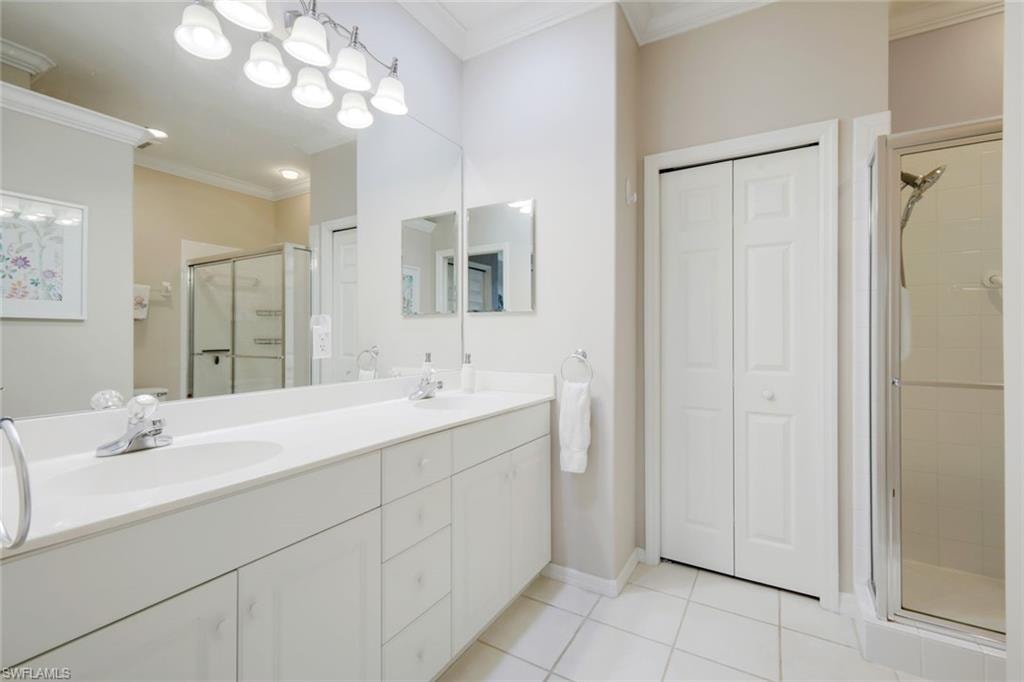 Full bath with a closet, double vanity, ornamental molding, a shower stall, and light tile patterned floors