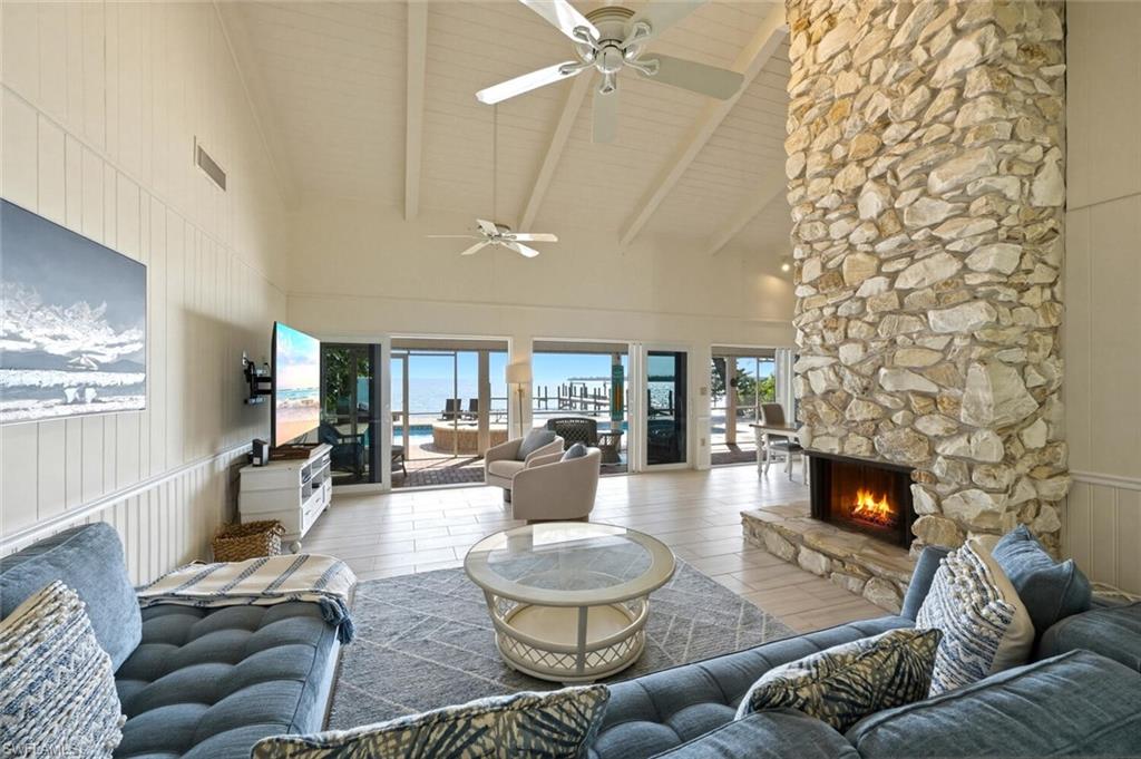 Living area with vaulted ceiling, a ceiling fan, wooden walls, a stone fireplace, and wood finished floors