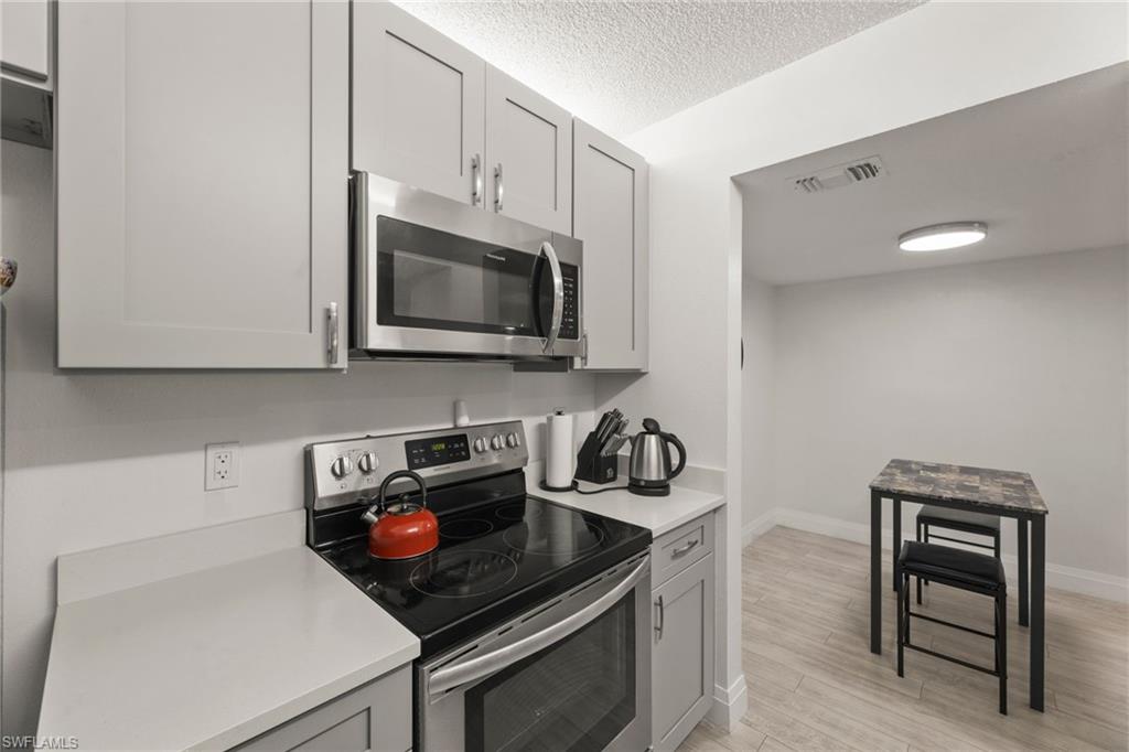 Kitchen with stainless steel appliances, gray cabinetry, light wood-style flooring, and a textured ceiling