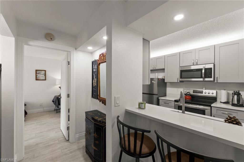 Kitchen featuring a breakfast bar, gray cabinetry, stainless steel appliances, light wood-style floors, and a peninsula