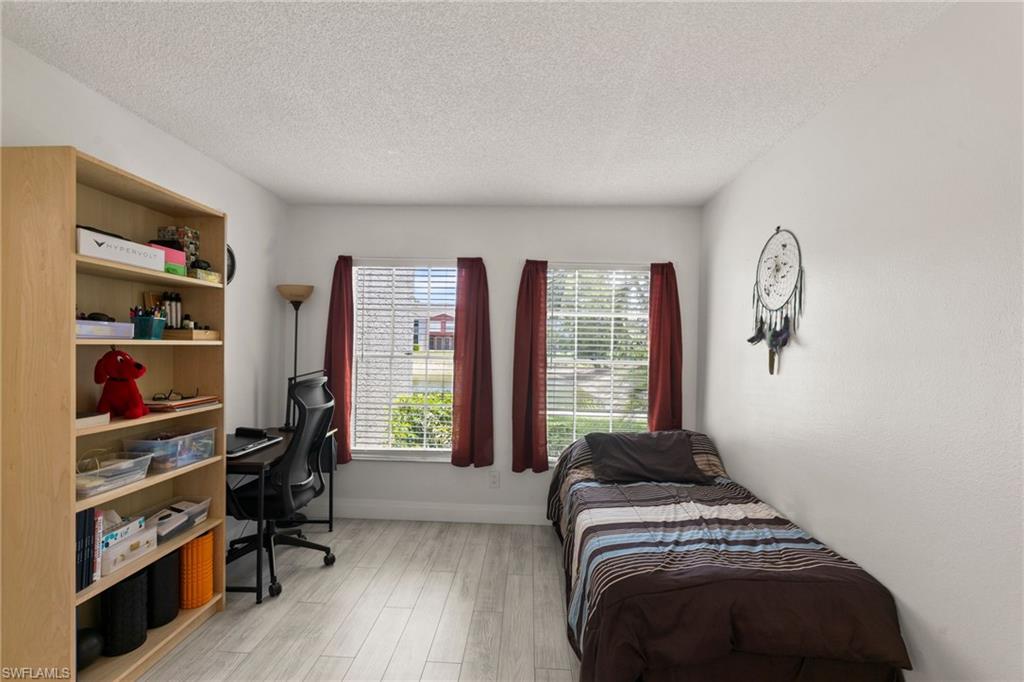 Bedroom with an office area, light wood-type flooring, and a textured ceiling