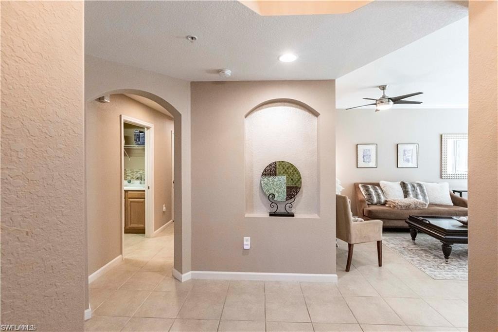 Hall featuring arched walkways, recessed lighting, light tile patterned floors, a textured wall, and a textured ceiling