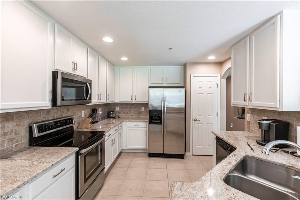 Kitchen featuring stainless steel appliances, light stone countertops, white cabinets, light tile patterned flooring, and recessed lighting