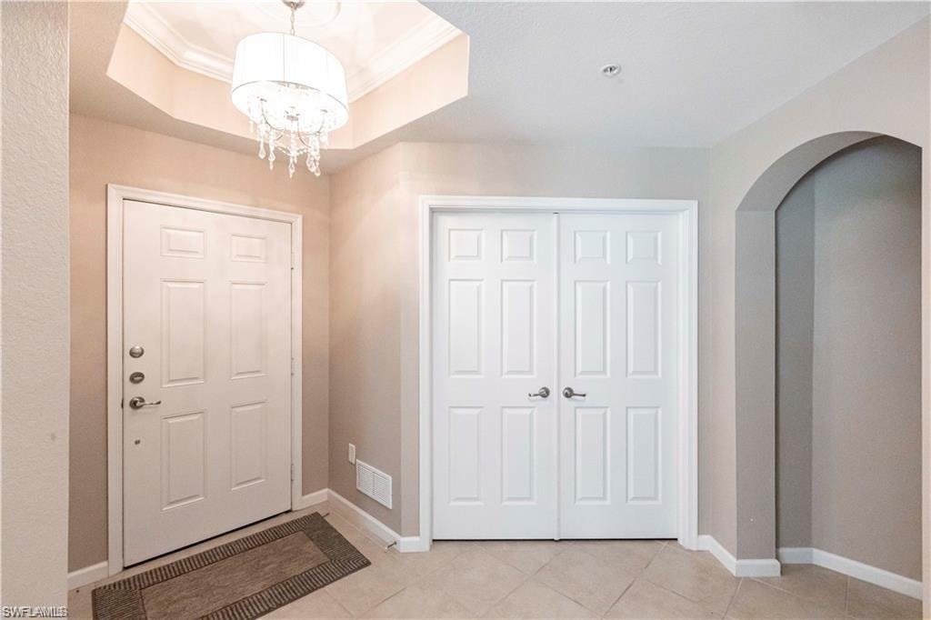 Foyer featuring light tile patterned flooring, ornamental molding, arched walkways, a raised ceiling, and a chandelier