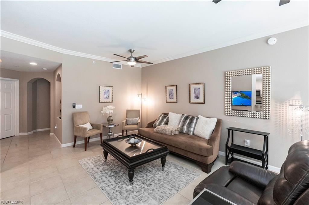 Living room with arched walkways, a ceiling fan, light tile patterned flooring, and ornamental molding
