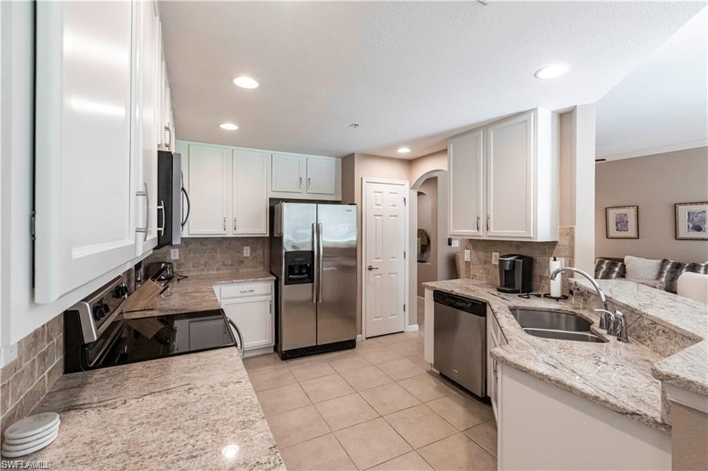 Kitchen featuring stainless steel appliances, decorative backsplash, light stone counters, white cabinetry, and light tile patterned flooring