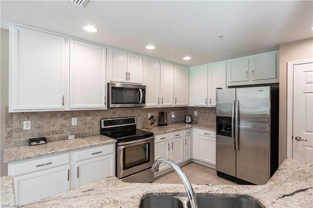Kitchen with stainless steel appliances, white cabinets, light stone counters, light tile patterned floors, and recessed lighting