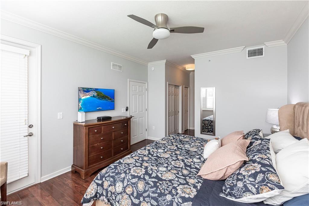 Bedroom with crown molding, dark wood-style floors, a ceiling fan, and multiple closets
