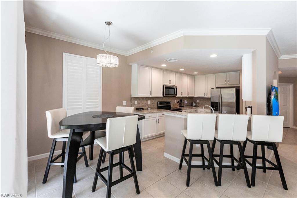 Kitchen featuring a breakfast bar area, crown molding, stainless steel appliances, light stone countertops, and decorative backsplash