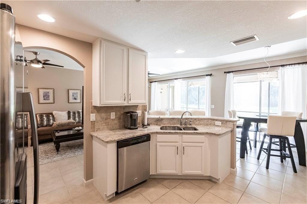 Kitchen with a peninsula, ceiling fan, light stone countertops, white cabinetry, and stainless steel appliances