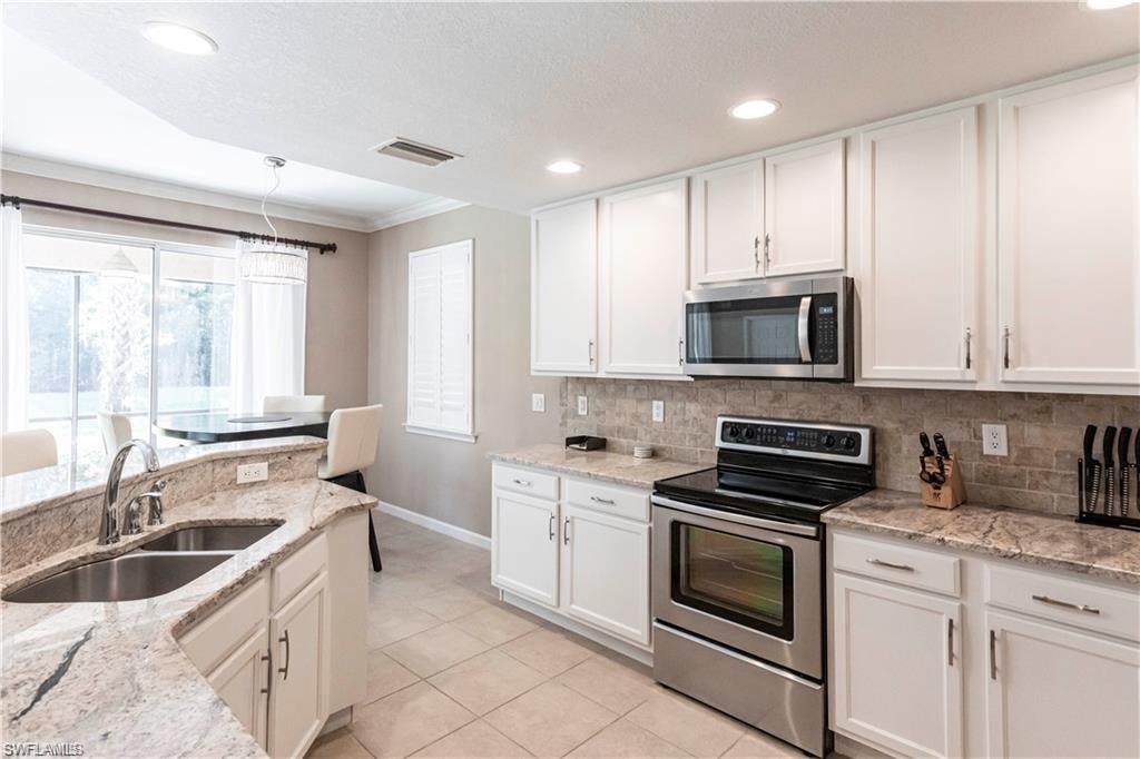 Kitchen with stainless steel appliances, white cabinets, ornamental molding, light stone counters, and tasteful backsplash