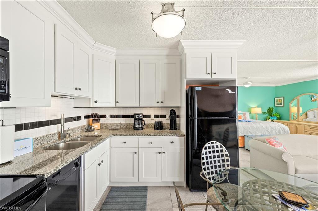 Kitchen with black appliances, white cabinets, a textured ceiling, open floor plan, and decorative backsplash