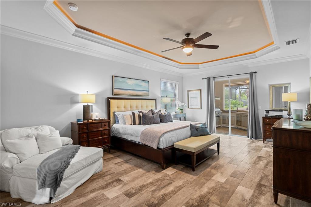 Bedroom featuring light wood-type flooring, a tray ceiling, ornamental molding, a ceiling fan, and access to exterior