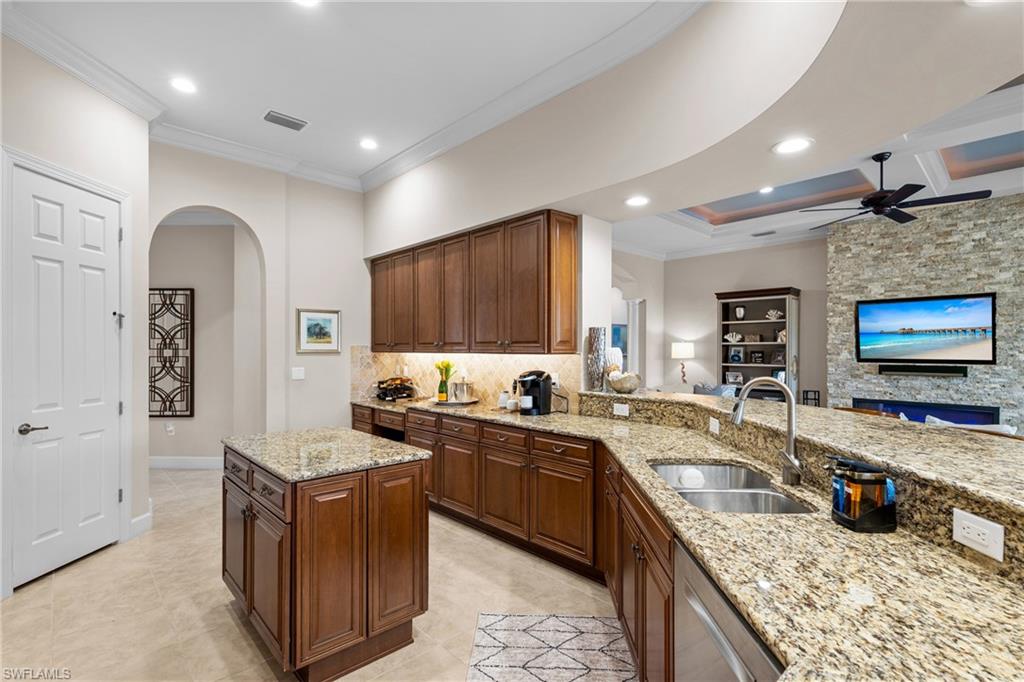 Kitchen with arched walkways, crown molding, light stone countertops, a ceiling fan, and dishwasher